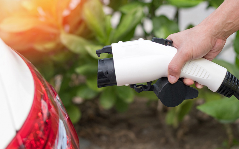 Hand holding an EV charger, ready to plug it into a vehicle.