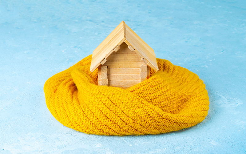 Conceptual image of a toy wooden house wrapped in a warm scarf